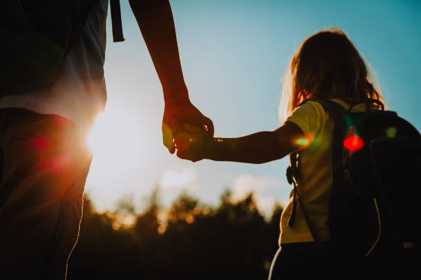 little boy and girl with backpacks holding hands at sunset sky